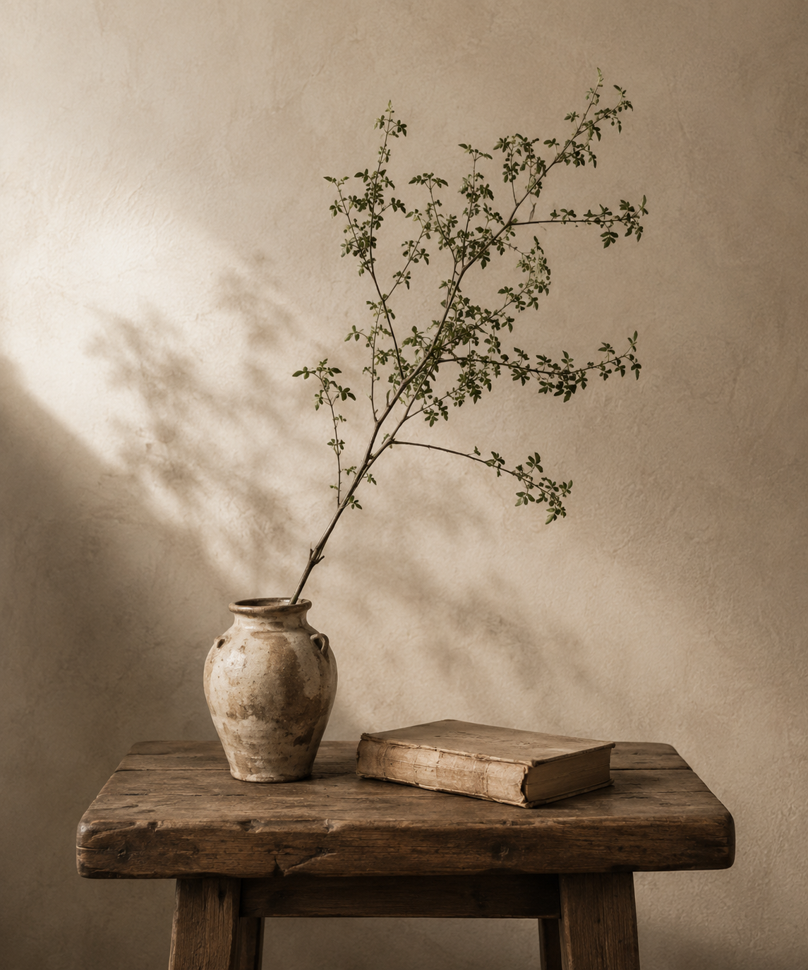 A vintage ceramic vessel and worn book on an antique wooden stool against a plaster wall